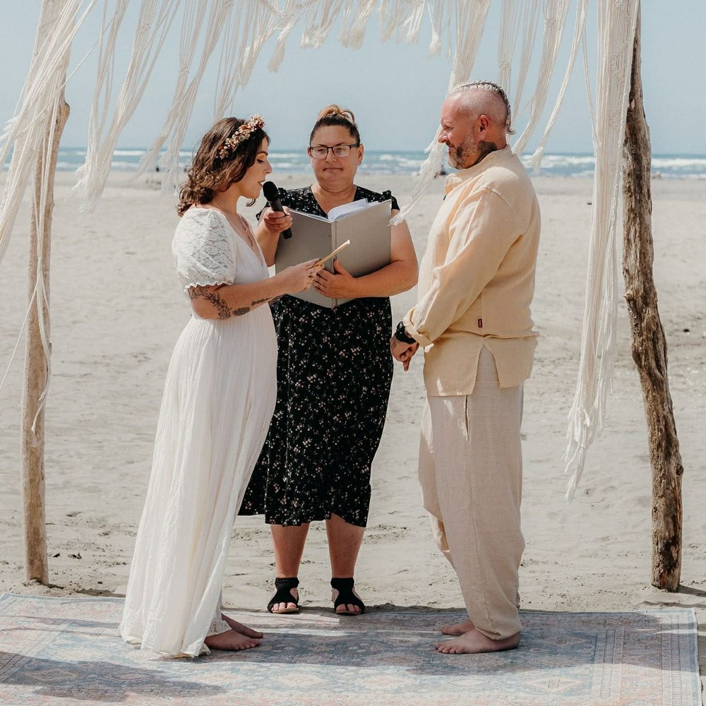 Danielle marrying a barefoot couple on the beach under a driftwood arch