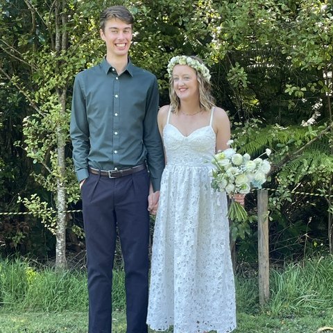 A smiling newly married couple holding hands, the bride with a flower crown and bouquet
